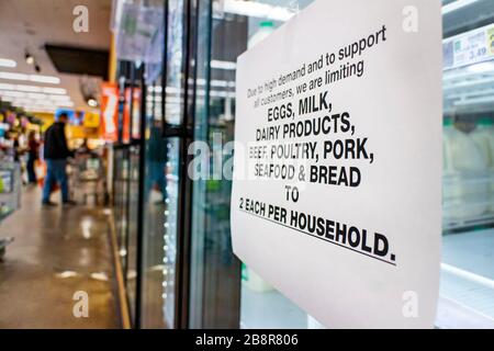 Coronavirus related sign rationing food such as dairy products ,meat,seafood,bread and eggs at a supermarket. The shelves of the cooler are fairly emp Stock Photo