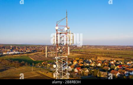 Elevated view of a cell tower, with satellite dishes, tv, radio and other telecommunication antennas on it. The small rural European city is sprawling Stock Photo