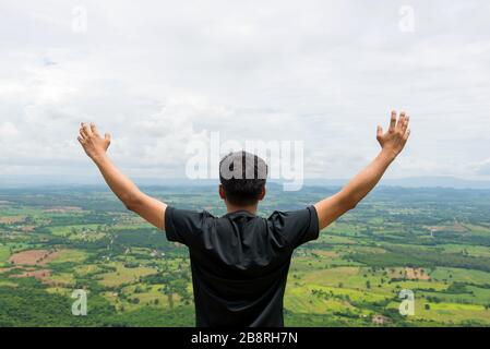 Young man standing on a mountain with raised hands and looking to view of landscape. Stock Photo