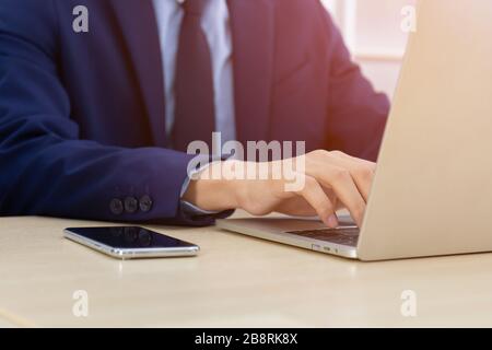 A man with a business man typing on a desk with a laptop Stock Photo