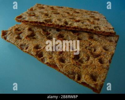 brown rustic thin rye crisp bread slice or cracker. rough textured grainy surface with bumps and holes. dark gray glass surface. healthy food concept Stock Photo