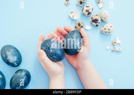 Children hands holding Easter blue color eggs close to eggshell on the light blue background. Top view. Easter concept. Stock Photo