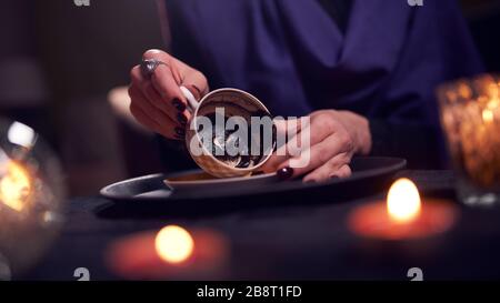 Female fortune teller divines on coffee grounds at table with ball of predictions in room Stock Photo