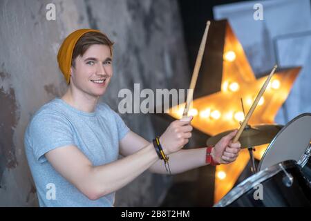 Young man in an orange hat smiling nicely playing the drums Stock Photo