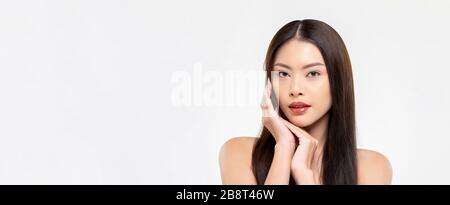 Banner beauty shot of confident Asian woman model with clear fair skin doing hands touching face pose in white isolated studio background with copy sp Stock Photo