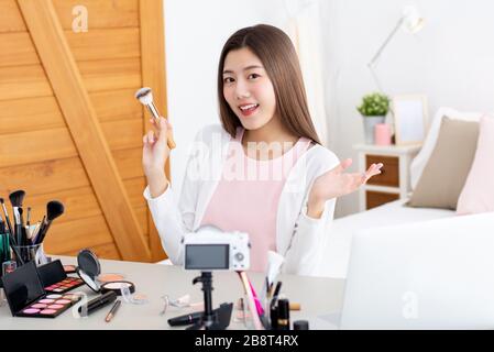 Young attractive asian woman beauty vlogger holding make up brush doing live streaming in front of camera Stock Photo