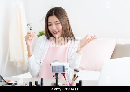 Young attractive asian woman beauty vlogger holding eyelash curler doing live streaming in front of camera Stock Photo