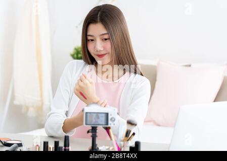 Young attractive asian woman beauty vlogger testing lipstick at the back of her hand in front of camera Stock Photo