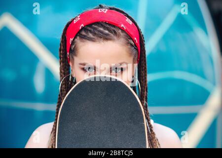 Close-up of portrait of hipster woman holding a longboard near her face in the city street Stock Photo