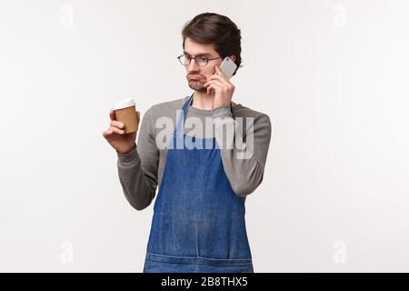 Portrait of unsure and indecisive young man having conversation on phone, drink coffee, grimacing puzzled, dont know, cant answer as have no idea Stock Photo