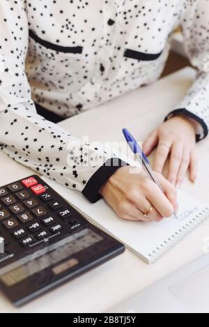 The girl is engaged in accounting. Woman's hand writes in a notebook home expenses and income. The concept of the distribution of cash, compliance with the family budget. Stock Photo