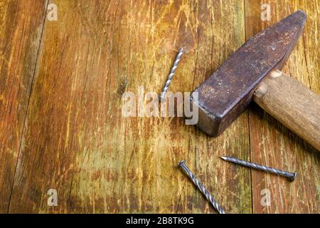 Old rusty hammer and three steel nails lie on a scratched wooden table. Copy space for text. Selective focus. Home work concept. Close-up. Stock Photo