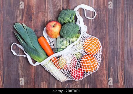 Textile string eco bag with fruits and vegetables on wooden background Stock Photo