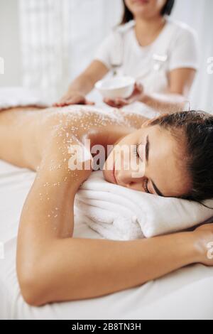 Beautician applying salt scrub on back of young woman Stock Photo