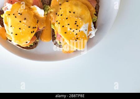 Toasts with avocado, salmon, poached egg and hollandaise sauce on a white plate. Stock Photo