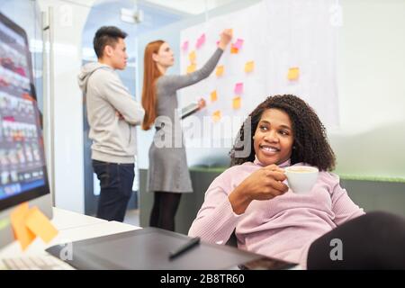 African woman as a trainee at the internet agency's computer takes a coffee break Stock Photo