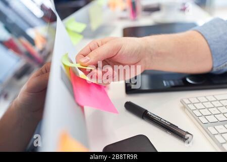 Hand of web designer or web developer sticks sticky notes on computer Stock Photo
