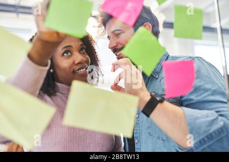 Two students or trainees brainstorming with sticky notes on glass wall Stock Photo
