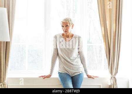 Cheerless senior female sitting on the sill Stock Photo