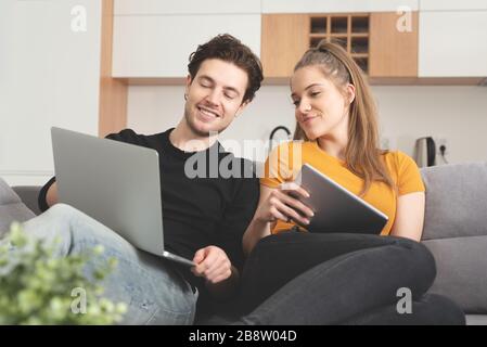 Couple using fast home internet with laptop and digital tablet. Woman and man on sofa in living room Stock Photo
