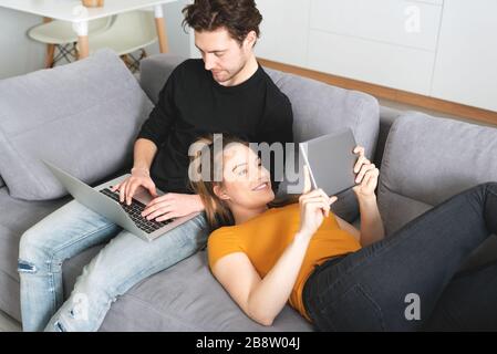 Couple using fast home internet with laptop and digital tablet. Woman and man on sofa in living room Stock Photo