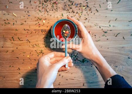 top view of female hands holding a teaspoon with tea leaves above a teacup on wooden table Stock Photo