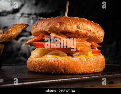 Appetizing fish burger with pieces of red fish meat on a brick wall background. Stock photo burger with fish filling. Stock Photo