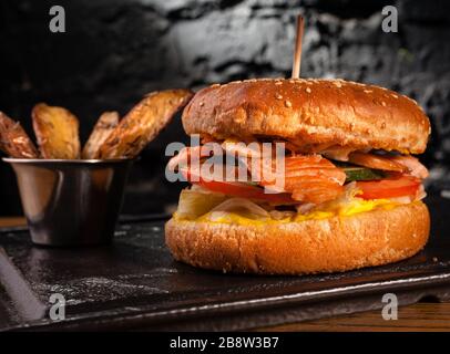 Appetizing fish burger with pieces of red fish meat on a brick wall background. Stock photo burger with fish filling. Stock Photo