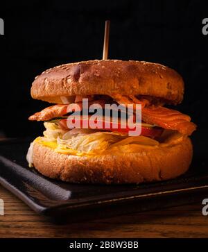 Appetizing fish burger with pieces of red fish meat on a brick wall background. Stock photo burger with fish filling. Stock Photo