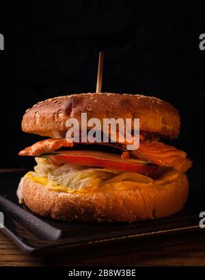 Appetizing fish burger with pieces of red fish meat on a brick wall background. Stock photo burger with fish filling. Stock Photo