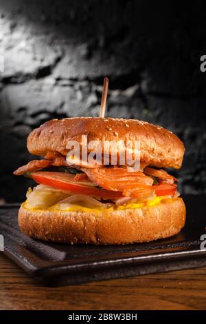Appetizing fish burger with pieces of red fish meat on a brick wall background. Stock photo burger with fish filling. Stock Photo