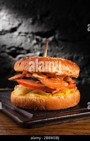 Appetizing fish burger with pieces of red fish meat on a brick wall background. Stock photo burger with fish filling. Stock Photo