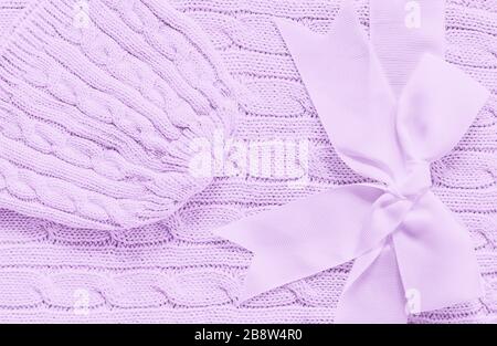 Baby knitted hat on a soft violet blanket. Cute gift for newborn baby with bow Stock Photo