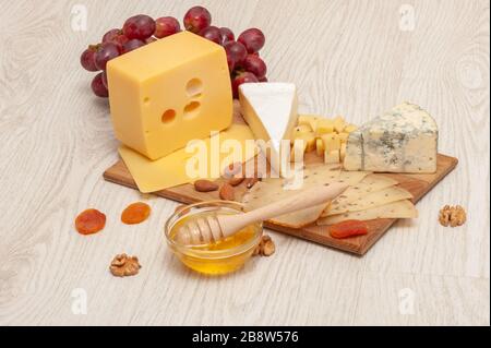 different types of cheese with nuts and dried apricots, grapes and honey on a wooden board. Top view Stock Photo