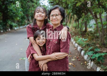 two asian granddaughters hugging their grandmother while playing in the park Stock Photo
