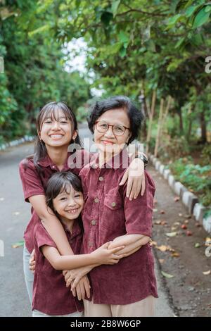 two granddaughters hugging their grandmother happily while playing in the park Stock Photo