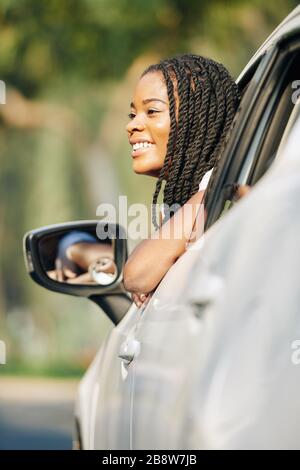 Lovely young African-American woman sticking out of car window when ordering food and drinks in drive through cafe Stock Photo