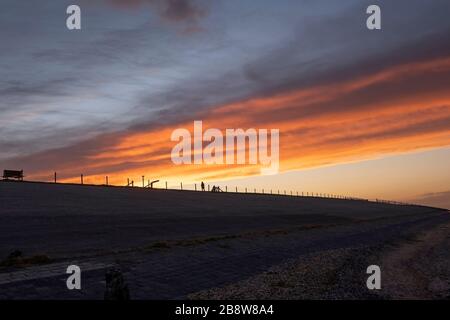 Beautiful colored cloudy skies in the colors blue, magenta, orange, purple and yellow at sunset in the Netherlands, autumn, a women silhouette against Stock Photo