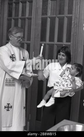 1970s, historical, baptism service, an infant child receiving a christian baptism, a traditional religious ceremony where an infant child's head being blessed with water. This is followed by a prayer welcoming the child into the family of the church, and a candle is presented to the child (mother) with the words 'Shine as a light in the world to the glory of God'. Stock Photo