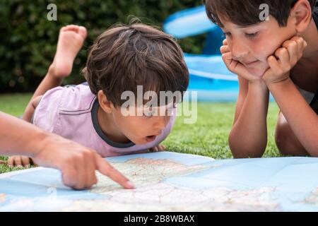Two boys sitting outdoors on a lawn, looking at a world map. Stock Photo