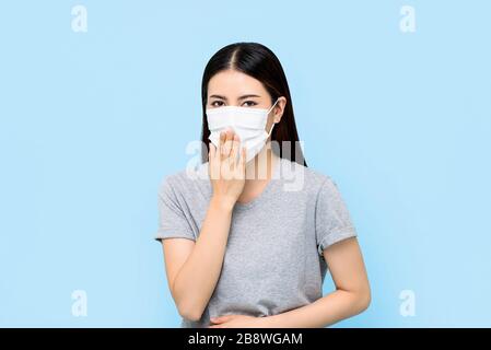 Asian woman wearing medical face mask coughing isolated on light blue background
