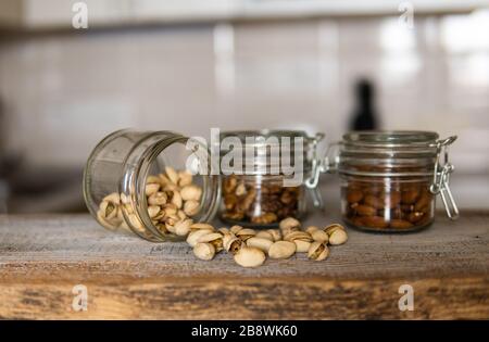 Pistachios scattered on the white vintage table from a jar and with other nuts on background. Pistachio is a healthy vegetarian protein nutritious Stock Photo