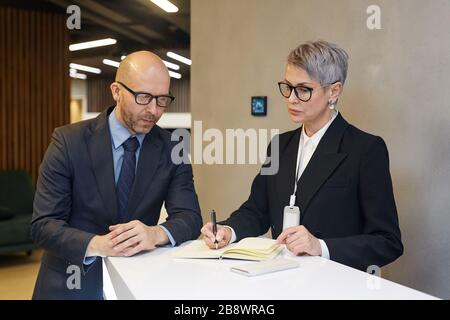 Waist up portrait of two mature business people writing out data from smartphone at stand in minimal office interior Stock Photo