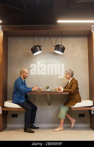 Side view full length portrait of two people sitting at table in indoor cafe during business meeting, copy space Stock Photo