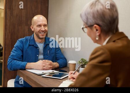 Portrait of mature bald man smiling happily while talking to business manager during meeting at cafe table, copy space Stock Photo