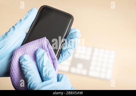 Hands with gloves cleaning mobile phone with disinfectant. COVID-19 Coronavirus outbreak contamination prevention concept Stock Photo