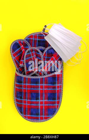 Set of checkered home slippers and several protective medical masks on yellow background. Hospitality and home protect on pandemic coronavirus Covid-1 Stock Photo