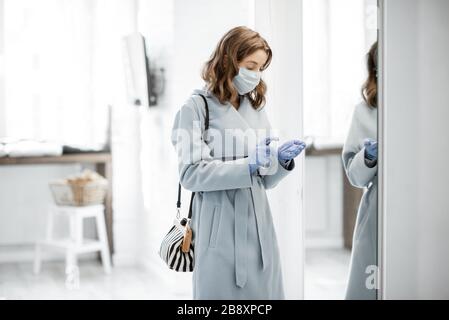 Woman in medical mask and gloves disinfecting hands after coming home from the street. Concept of prevention of virus spread during an epidemic Stock Photo