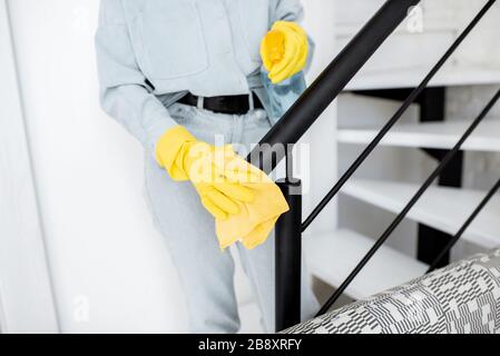 Woman in protective gloves disinfecting stair railings while cleaning at home, close-up view on hands Stock Photo