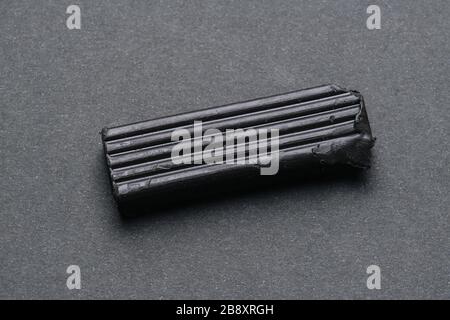 Black bar of plasticine on dark grey surface. High angle, close up. Stock Photo